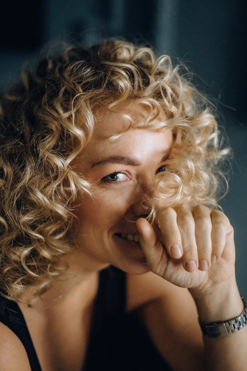blonde haired woman smiling with her hand on her face